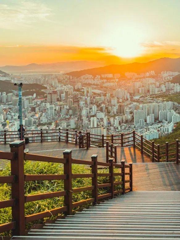 Wooden observation deck at Hwangnyeongsan glowing in golden sunset light above Busan's skyline
