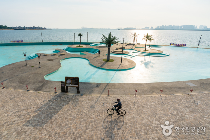 Turquoise waterfront terrace beside the calm Yellow Sea with a cyclist crossing the promenade
