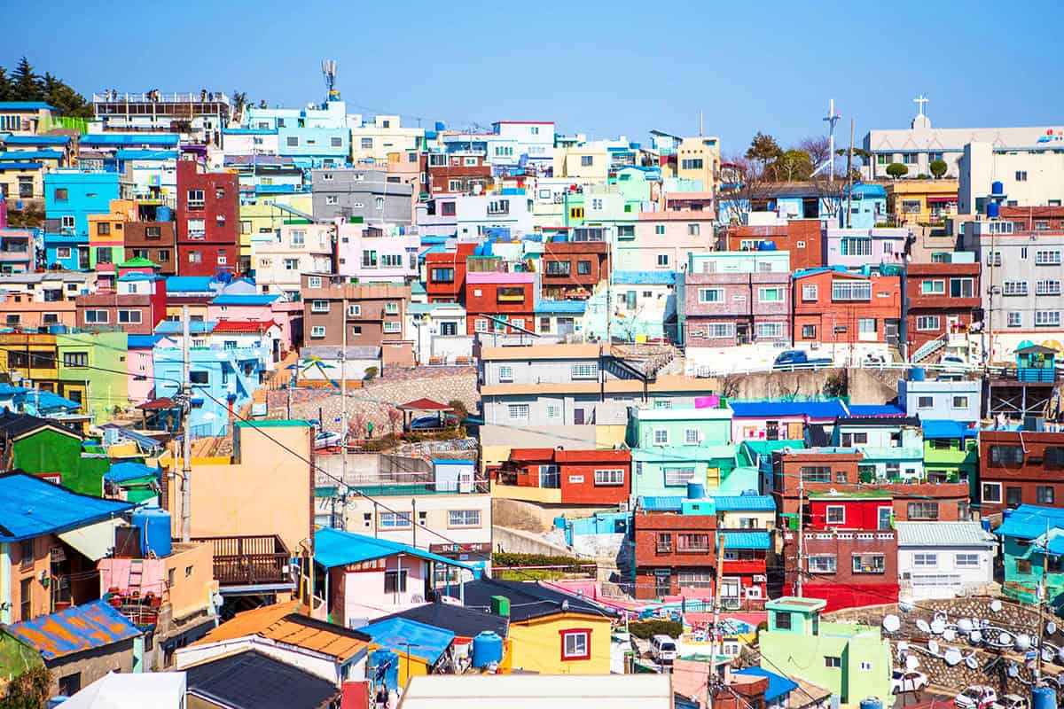 Colourful pastel houses stacked across the hillside of Gamcheon Culture Village under a blue sky