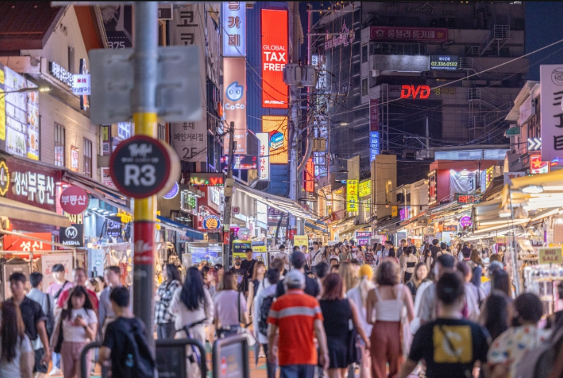 Crowds walking beneath colourful signs on a lively Hongdae street at night